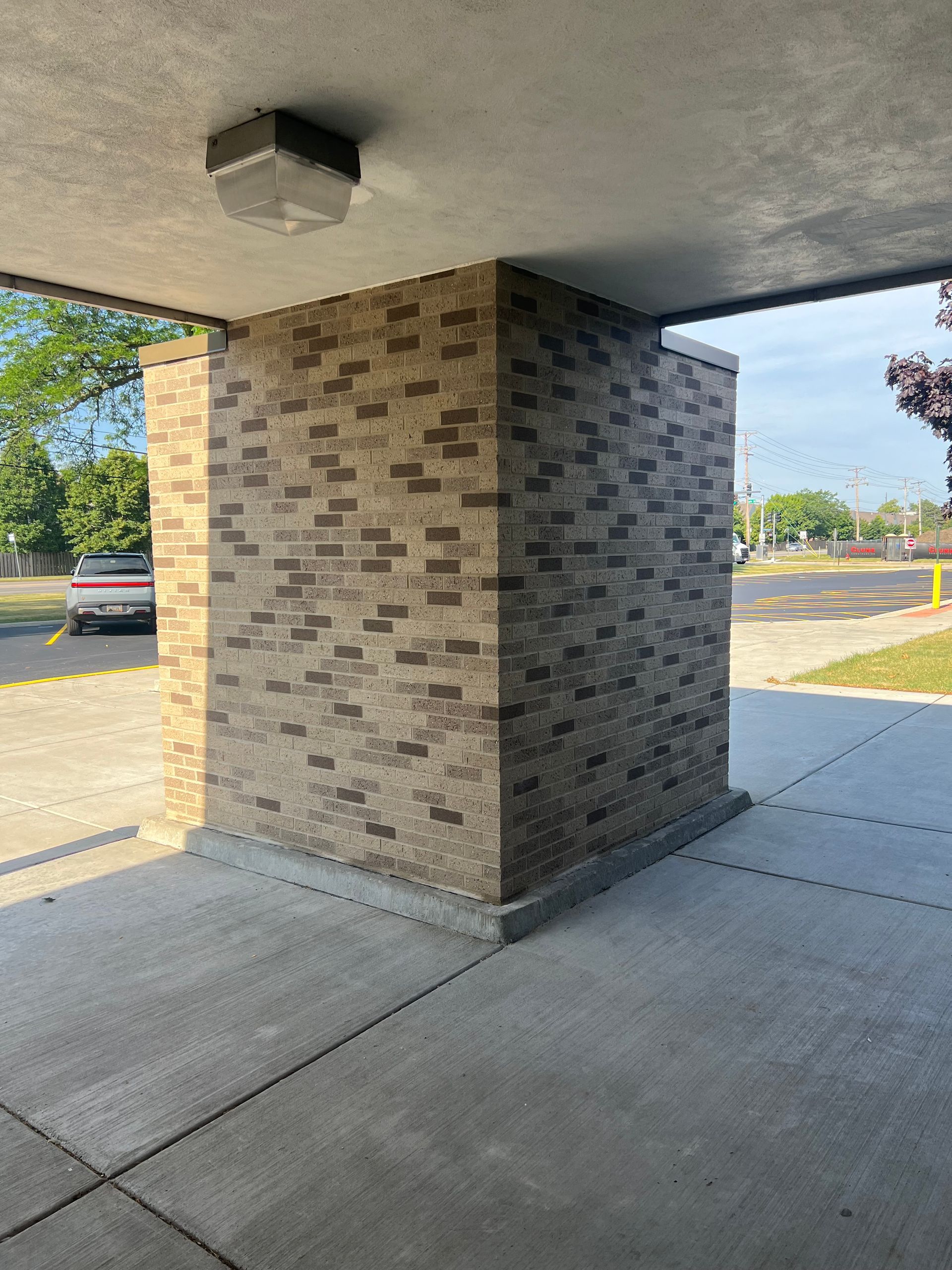 Brick pillar under a covered walkway beside a concrete sidewalk and parking lot.