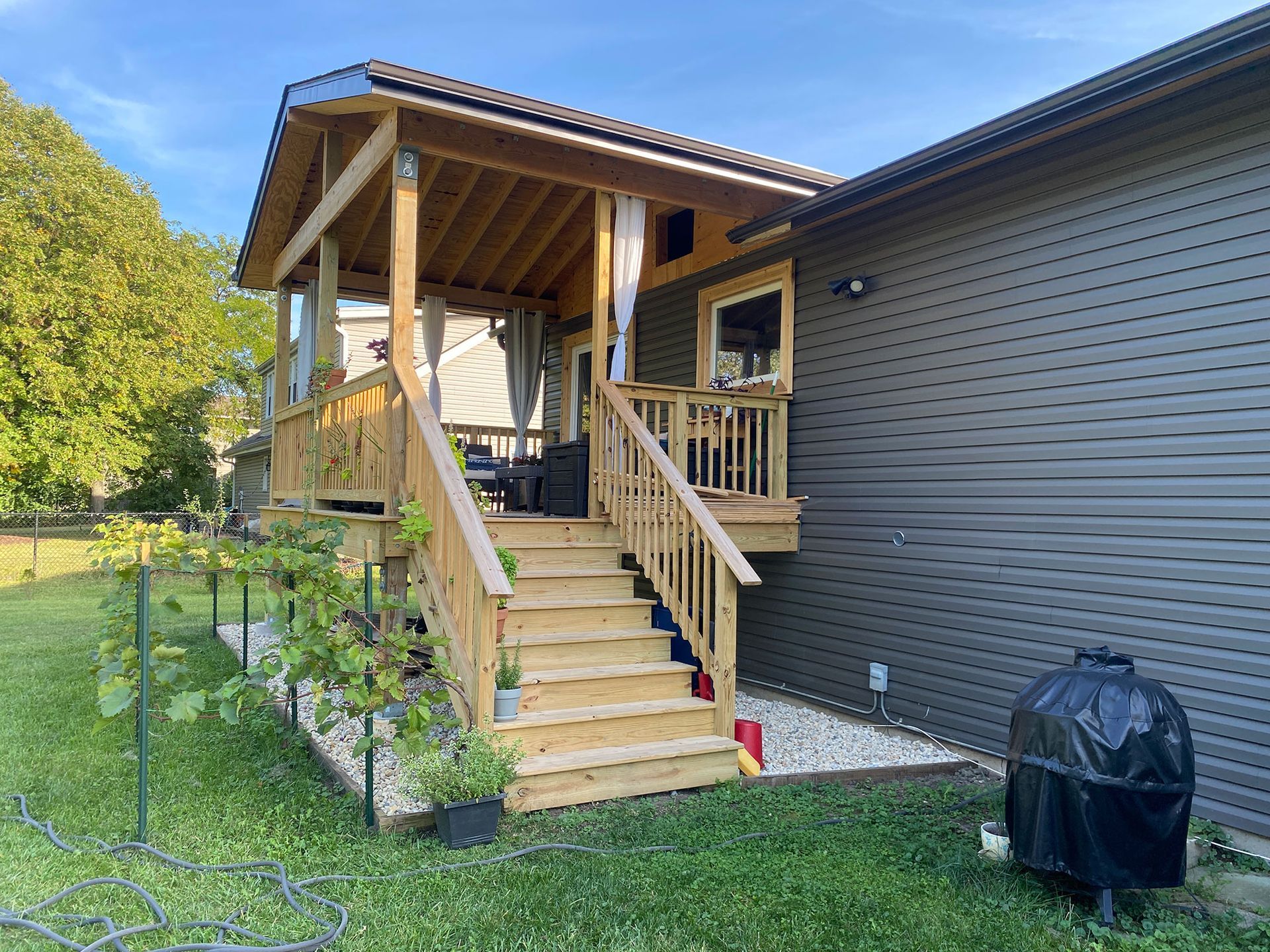 Wooden porch stairs with railings leading to a covered deck beside a dark-sided house.