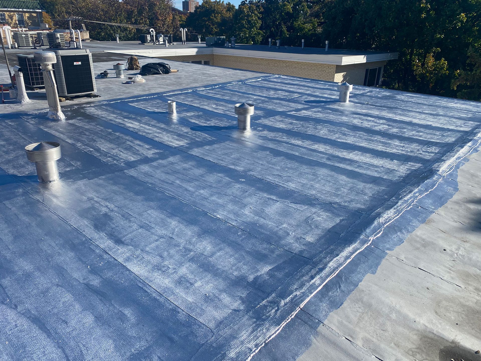Blue-coated flat rooftop with vents and HVAC units under daylight