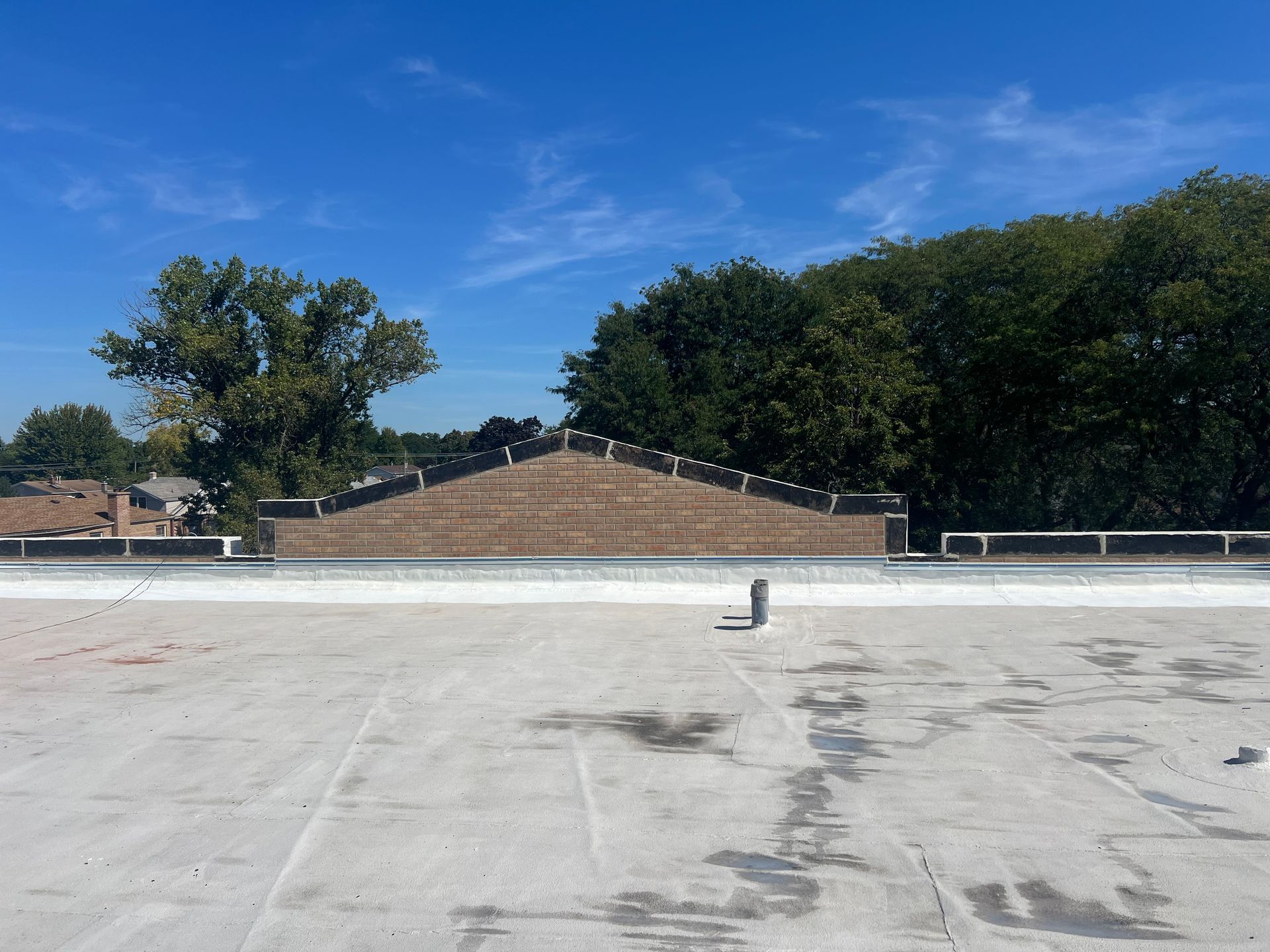 Empty rooftop with a small vent, brick wall, and trees under a clear blue sky