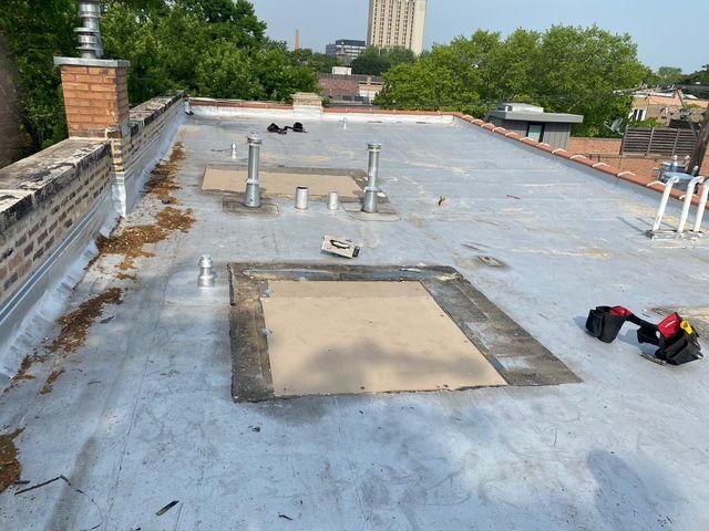 Flat rooftop with vents, pipes, a skylight, and rooftop maintenance tools under a cloudy sky.