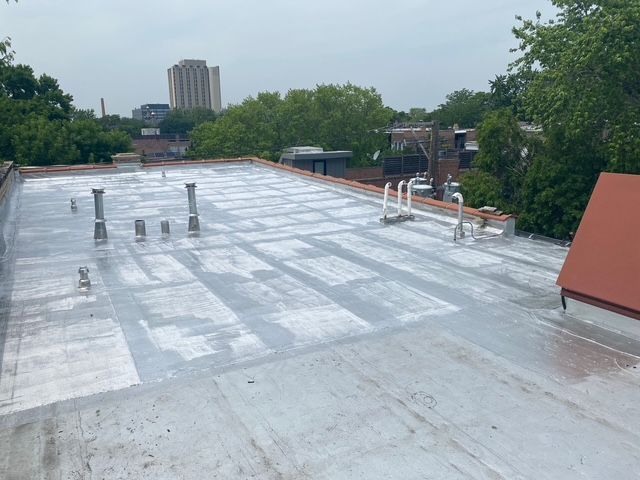 Flat rooftop with gray waterproof coating, vents, and trees under a cloudy sky