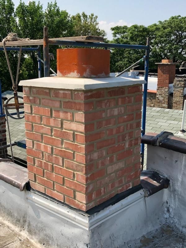 Brick chimney on a rooftop, capped with a white slab and orange flue pipe.