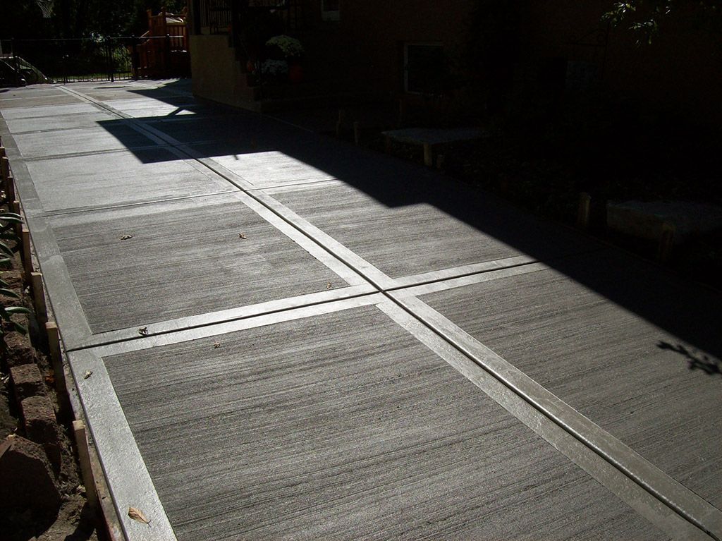 Sunlit sidewalk with white tactile paving strips and dark shadows alongside a building