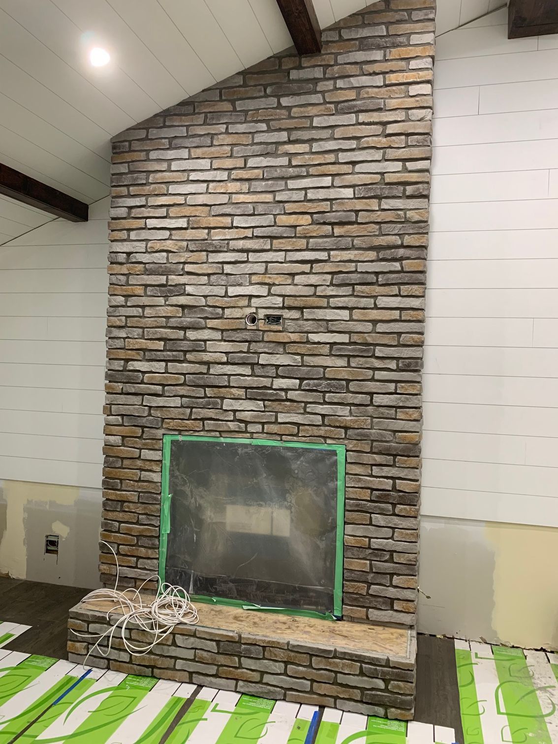 Brick fireplace wall with a green-taped opening in a room with sloped ceiling and white walls