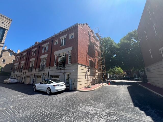Red brick building with white trim beside a parked white car in a sunny courtyard.