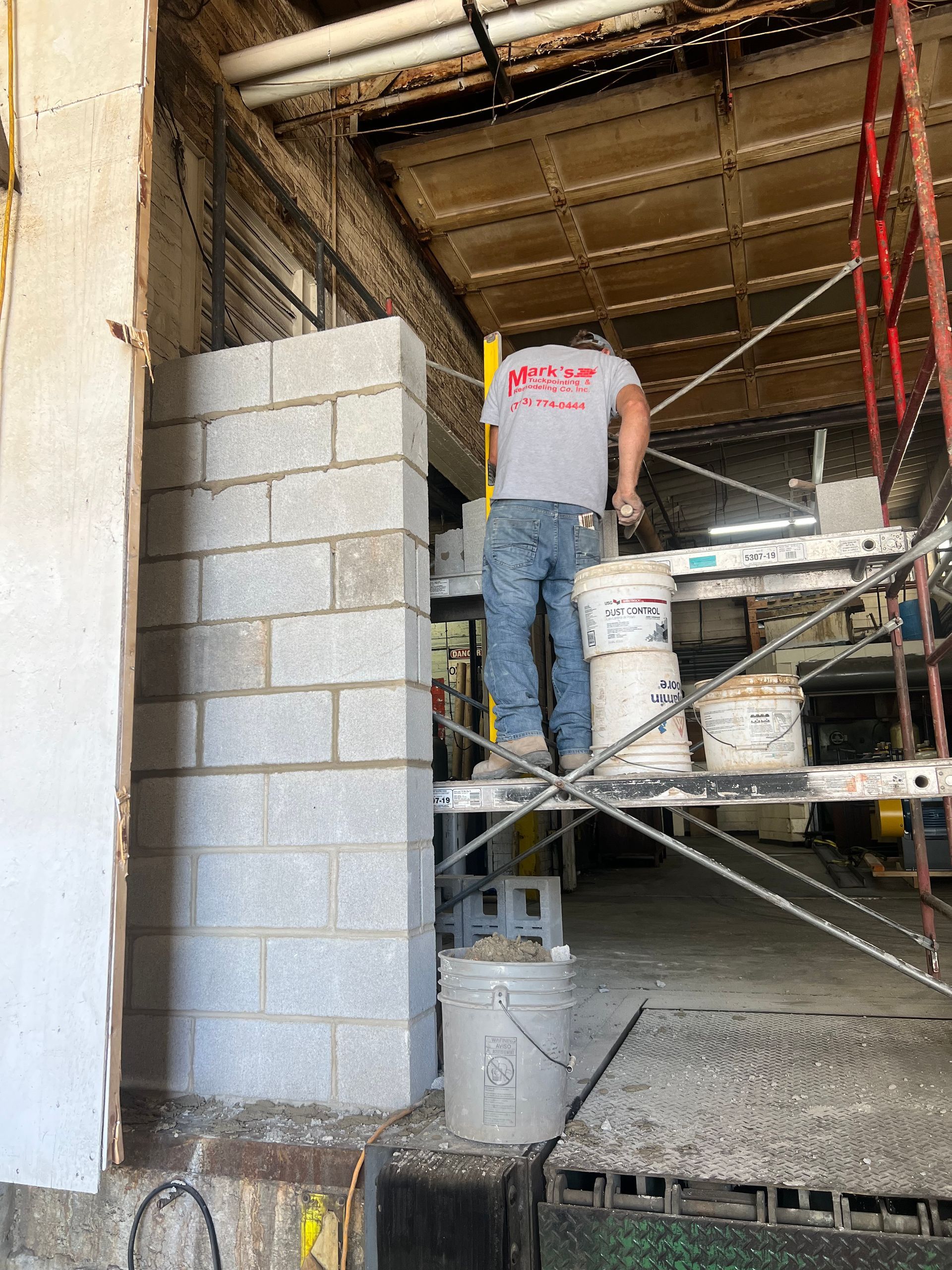 Worker on scaffolding stacking cinder blocks in a construction site doorway
