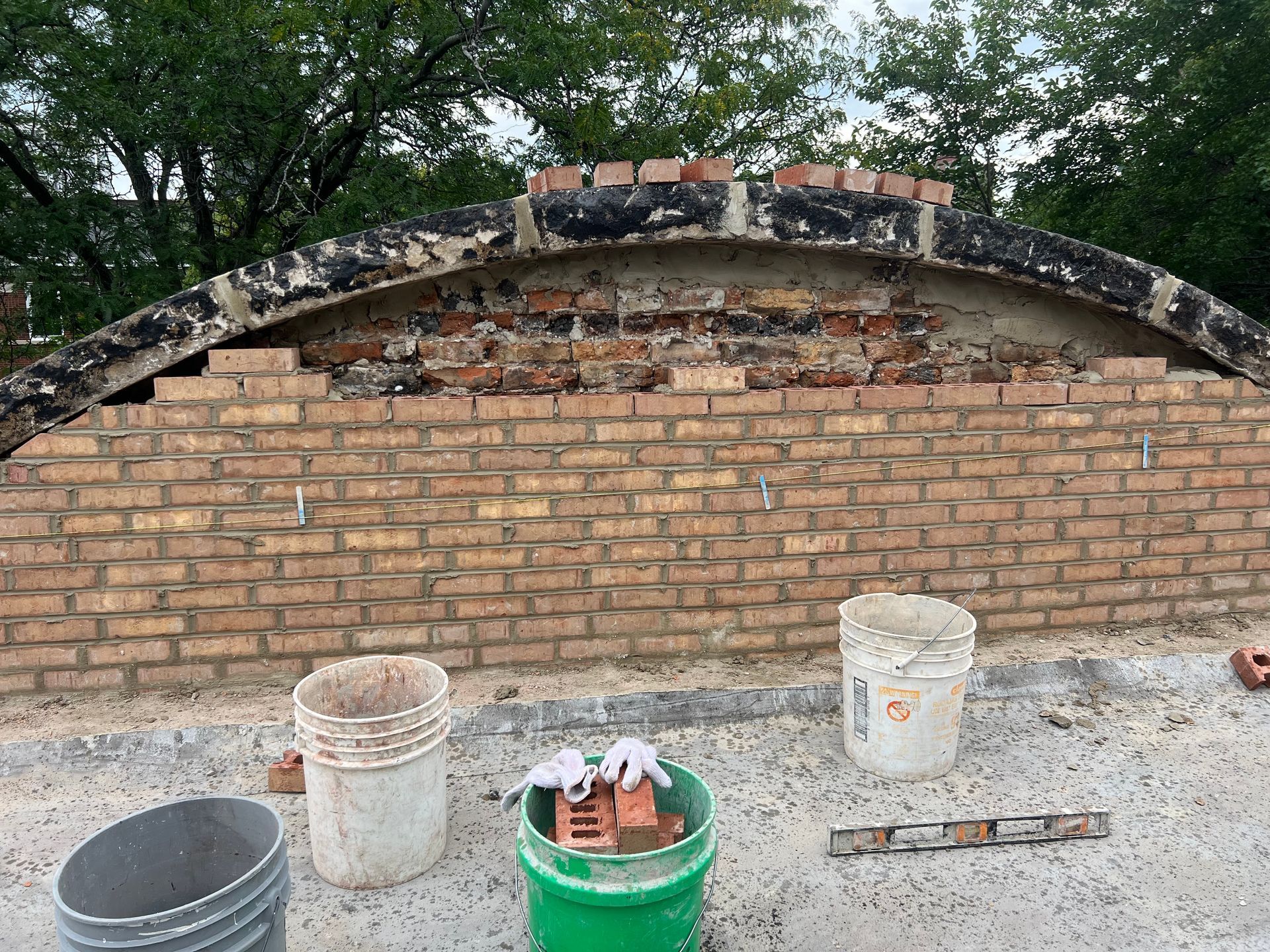 Brick wall under construction with three buckets and a green container on a concrete surface