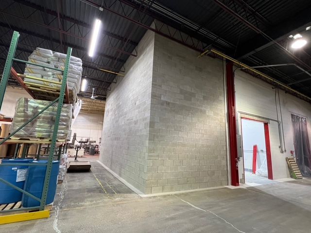 Warehouse interior with concrete block wall, stacked pallets, and an open doorway under industrial lighting