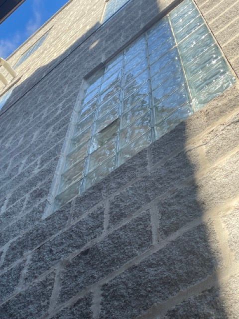 Tall stone building facade with a large reflective glass window and shadows cast across it