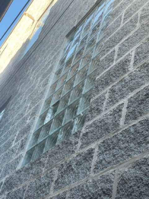 Angled view of a brick wall with a row of glass blocks near the top under a blue sky.