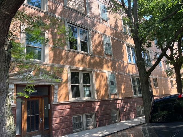 Brick apartment building with windows, entrance, and trees casting shadows on the facade