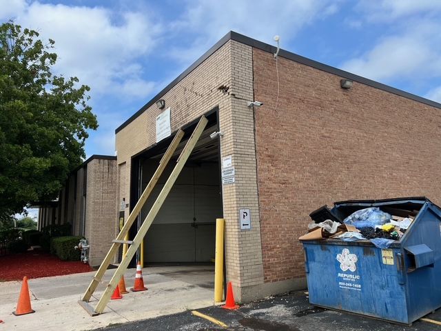 Dumpster and boarded garage entrance at a brick building, with cones and wooden supports.