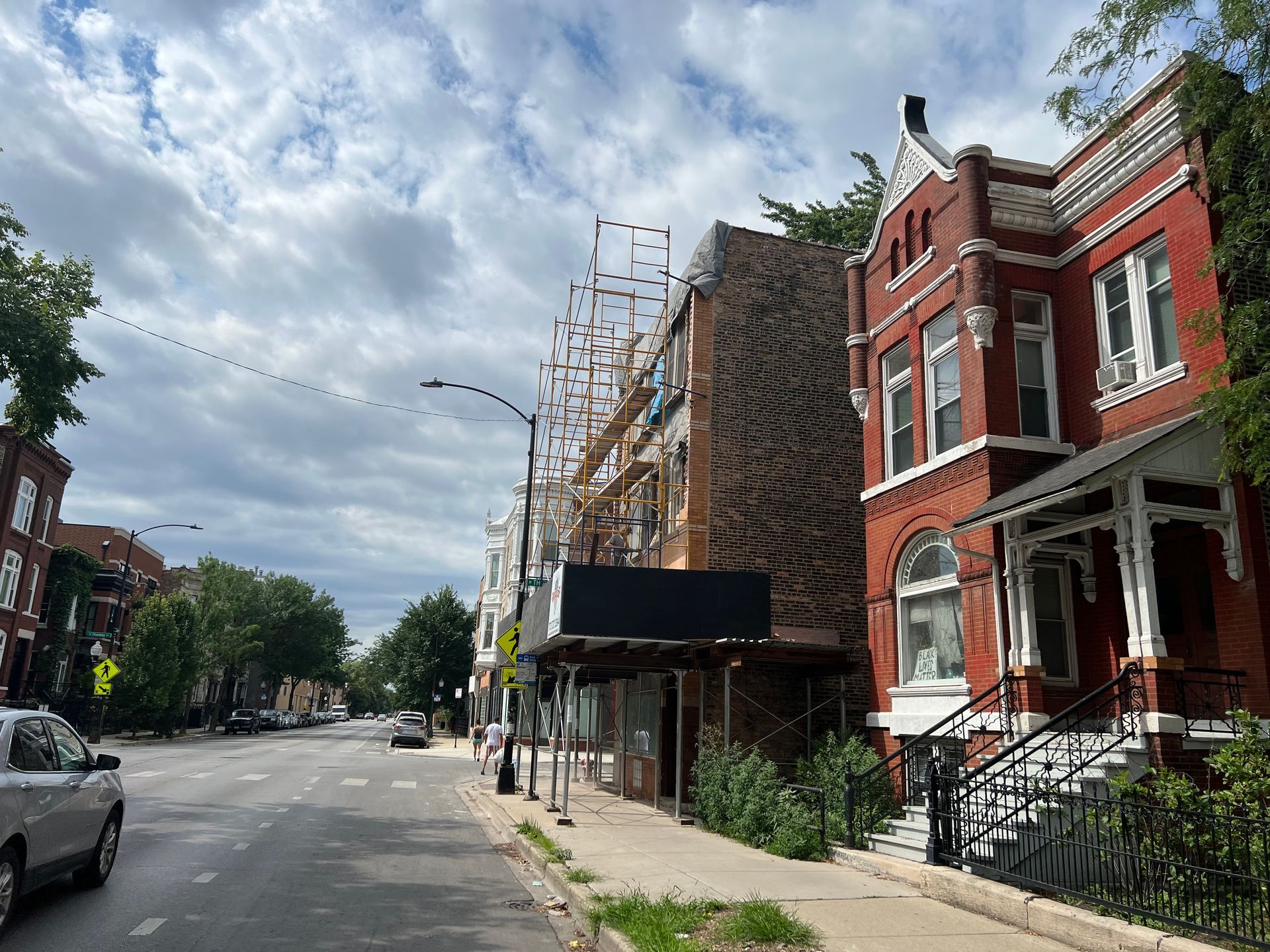 Quiet urban street with red-brick row houses, parked cars, and cloudy sky
