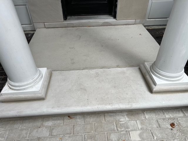 Front porch entrance with white columns, concrete steps, and a dark open doorway.