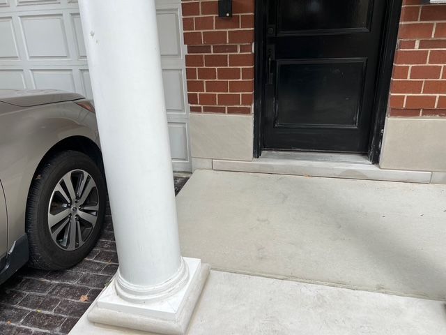 Front porch with white column, brick wall, black door, and a parked gray car beside the driveway.