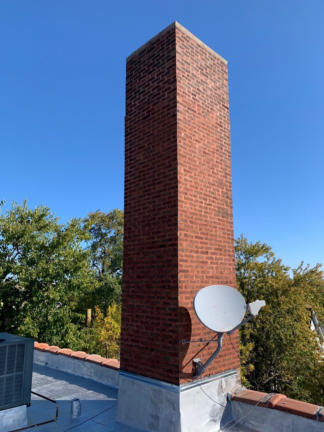 Brick chimney with a white satellite dish on a rooftop under a blue sky.