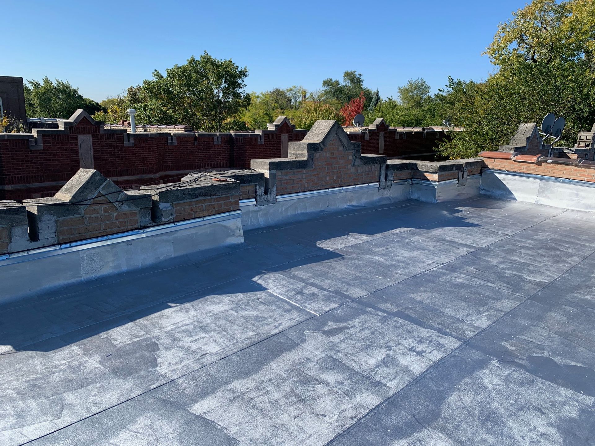 Rooftop with blue waterproof coating and low brick parapet walls under a clear sky