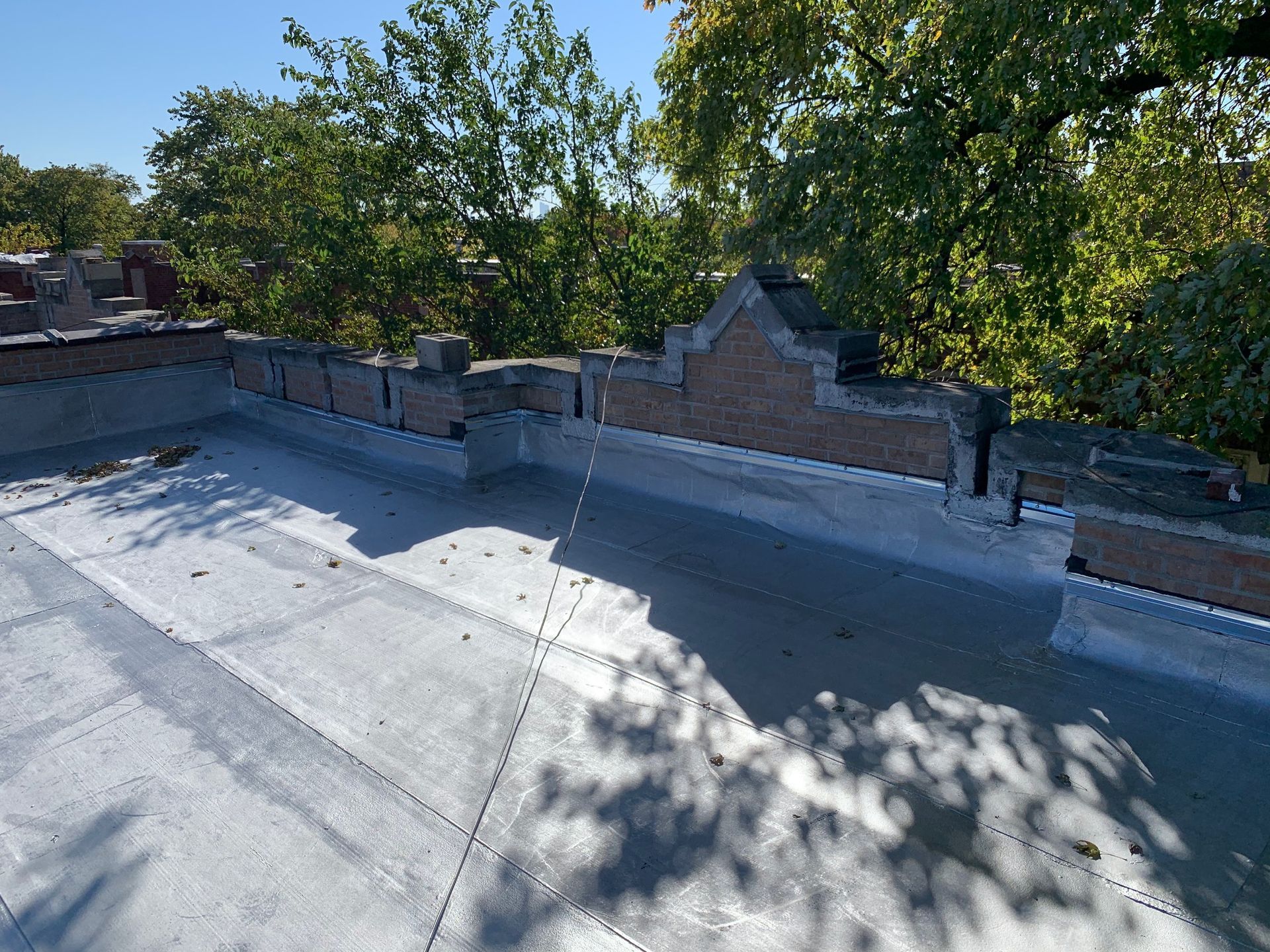 Rooftop with white membrane, brick parapet, and trees casting shadows on a sunny day