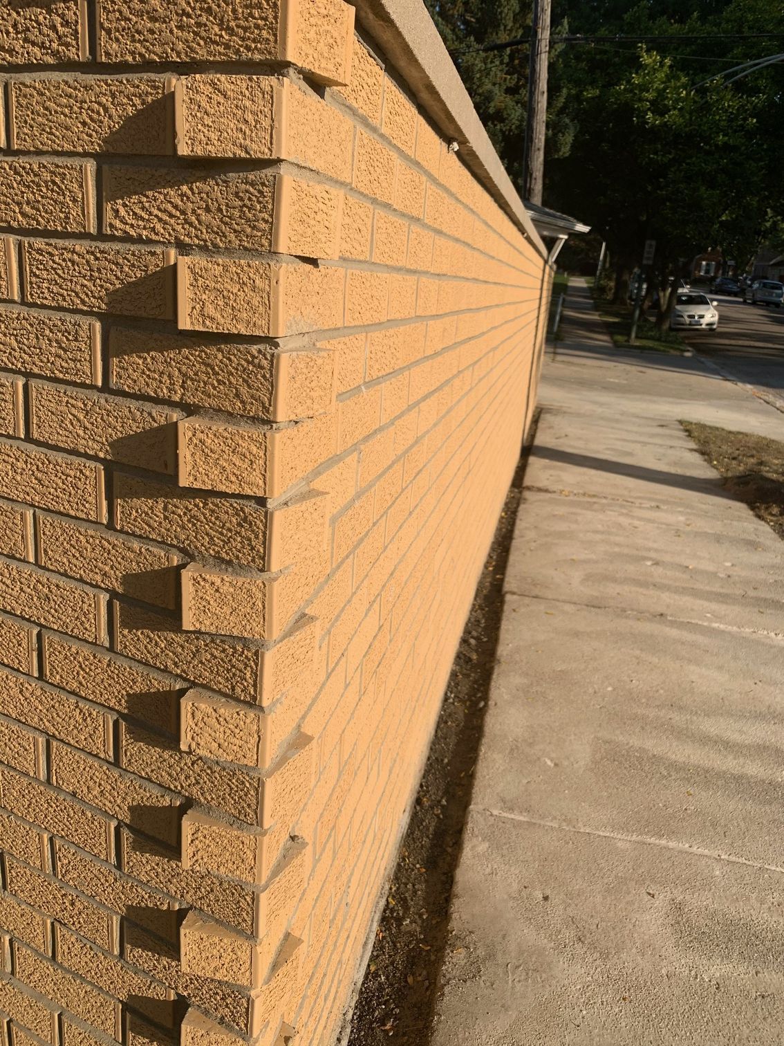 Corner of a tan brick wall along a sidewalk in bright sunlight