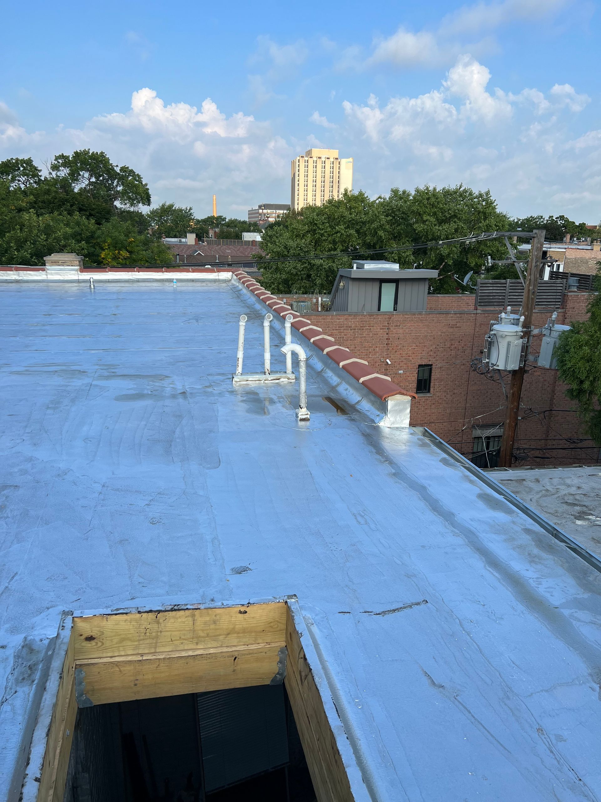 Blue rooftop with a skylight, brick building, trees, and a tall yellow tower under a partly cloudy sky