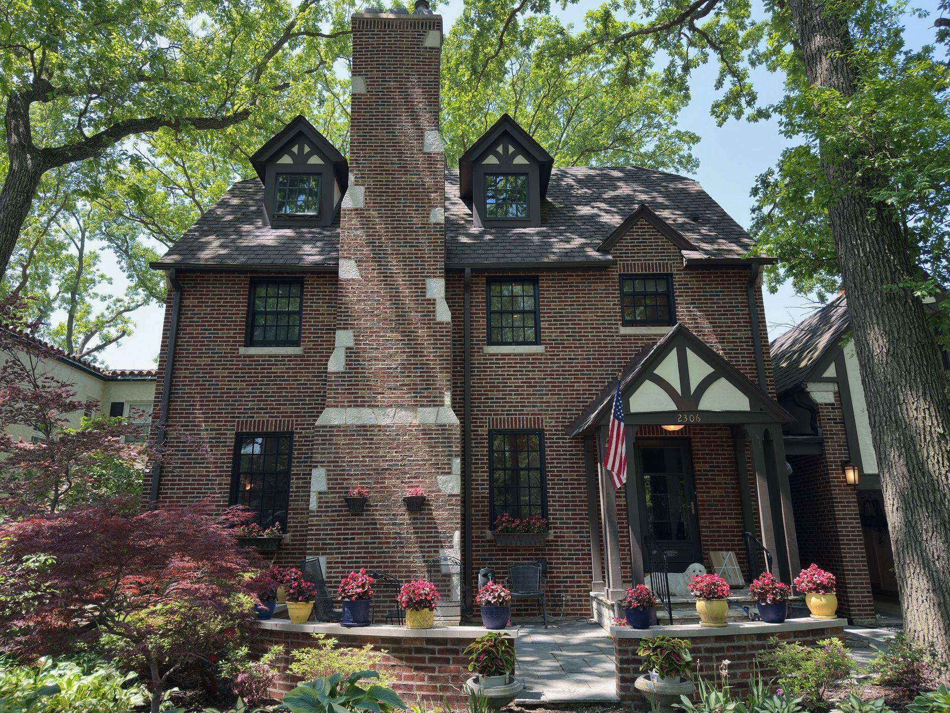 Brick Tudor-style house with tall chimney, green-trimmed windows, and flower planters by the front entrance