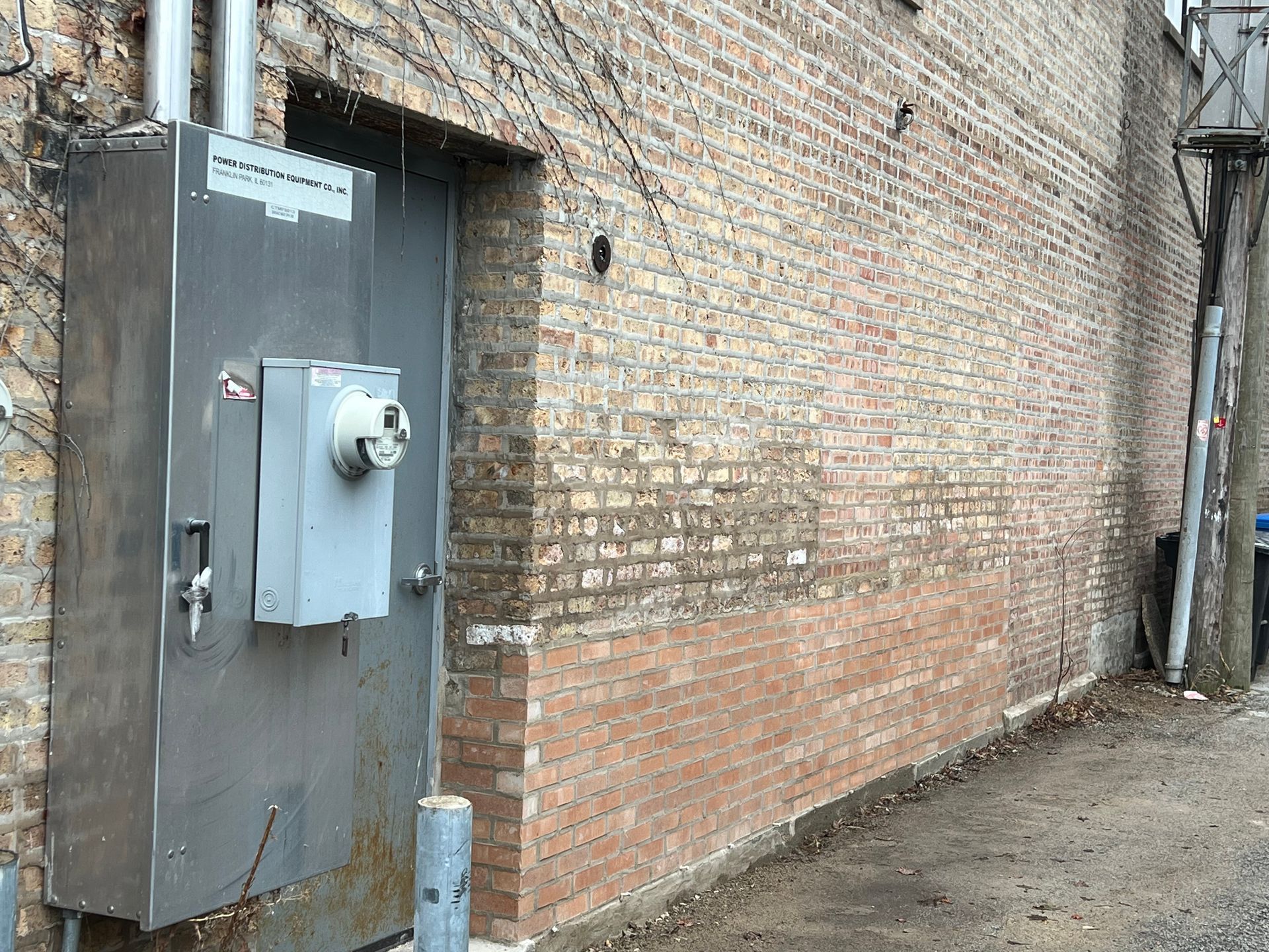 Alley beside a brick wall with a large metal utility door and electrical meter box.