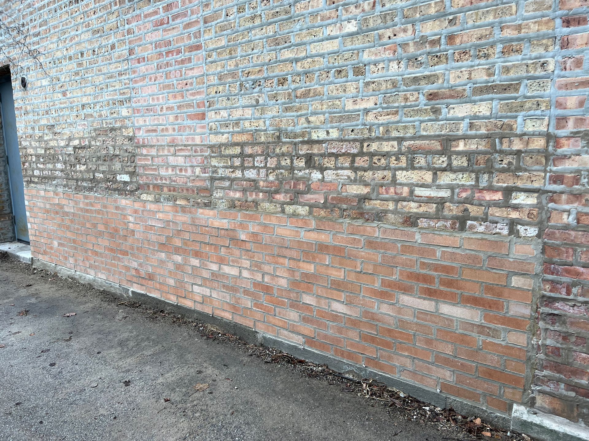Brick wall with faded paint beside a gravel ground and a dark doorway on the left