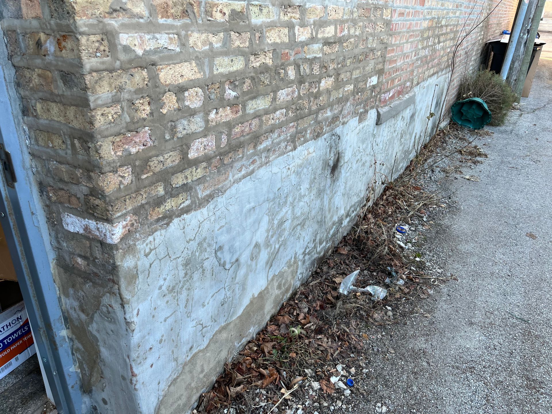Brick wall with peeling white paint beside a gravel path and debris along the base.