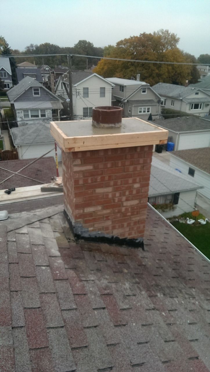 Brick chimney on a shingled rooftop with a residential neighborhood in the background.