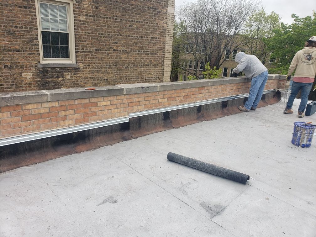Two workers installing brick edging along a patio beside a brick building.