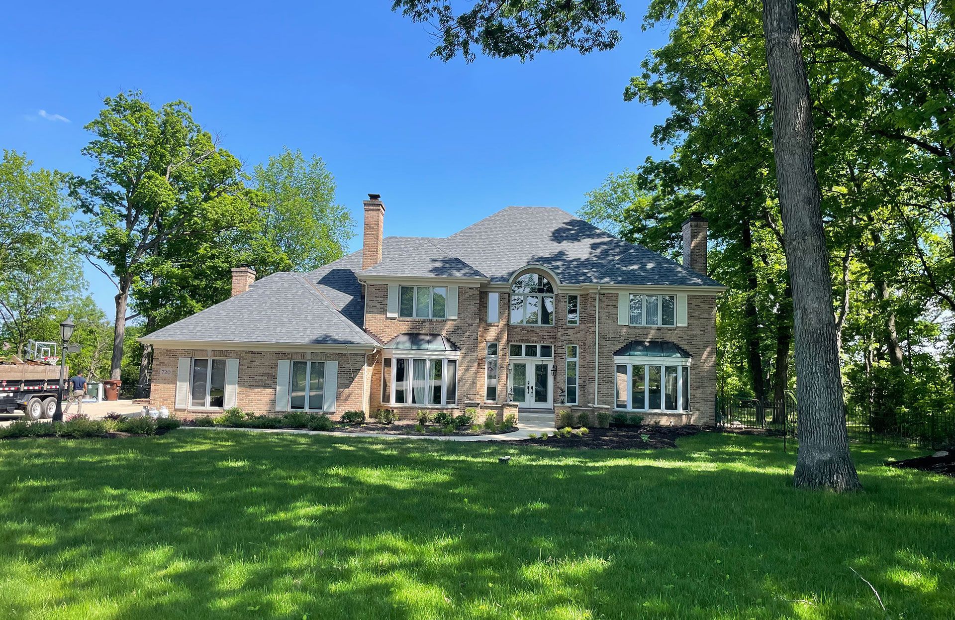 Large stone-and-brick house with a green lawn and trees on a sunny day