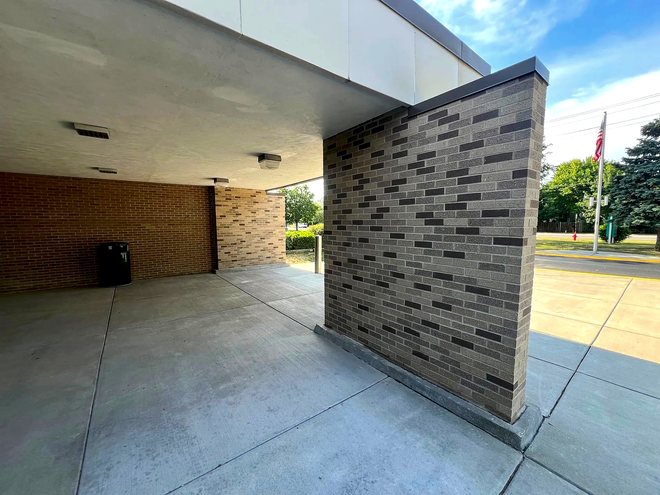 Covered walkway with brick columns and concrete floor outside a building