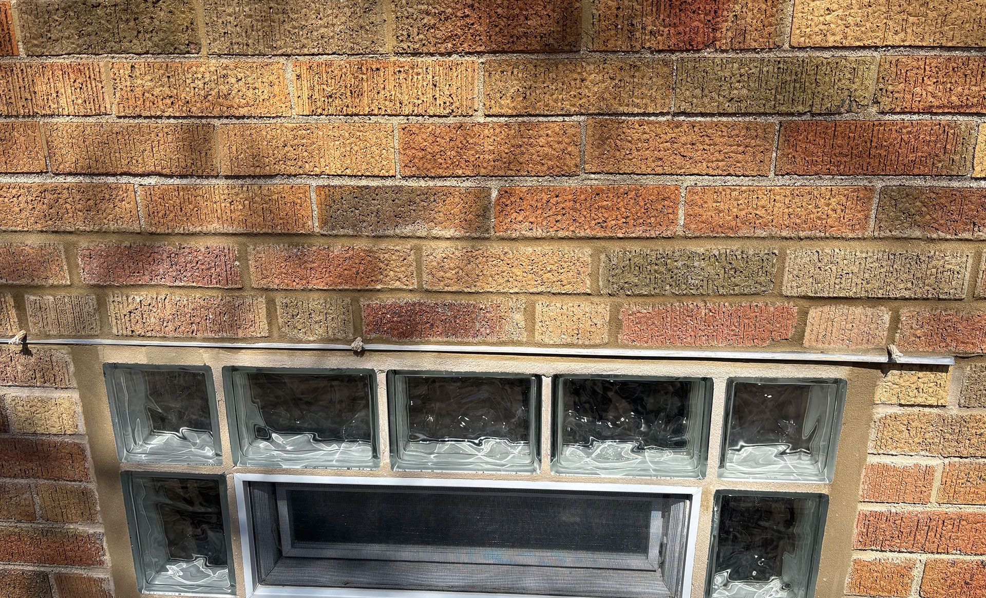 Brick wall with a small basement window and cracked concrete sill