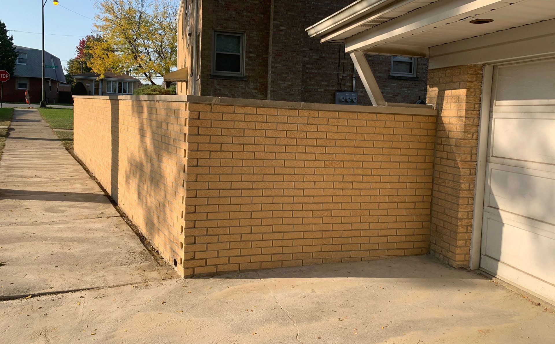 Brick wall beside a garage and sidewalk under a carport in daylight