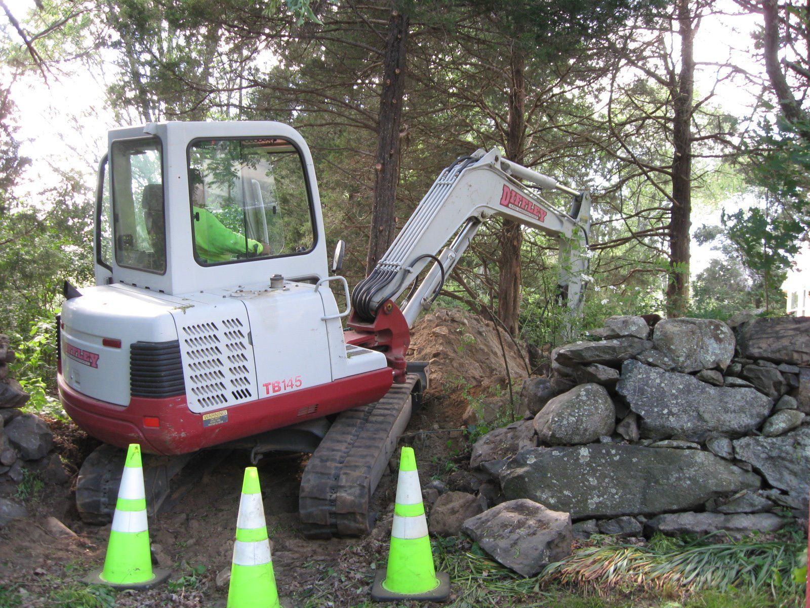 A white and red excavator is parked in front of a stone wall.
