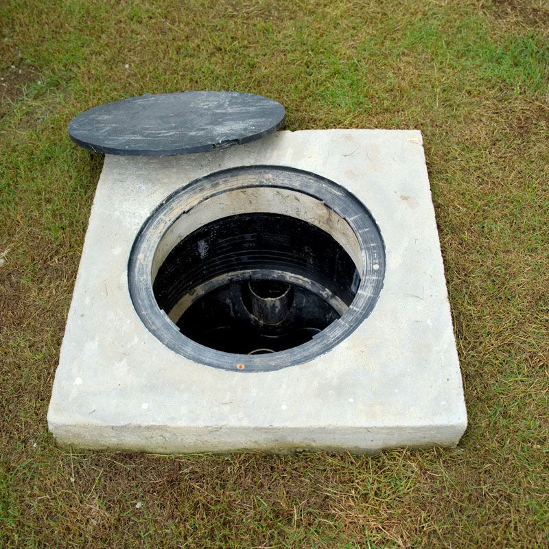 A manhole cover is sitting on top of a concrete slab in the grass.