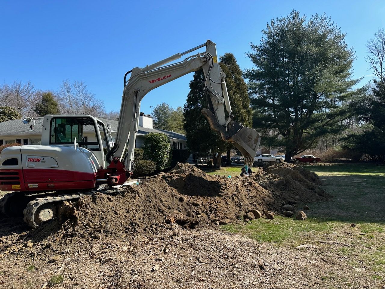 A white and red excavator is digging a hole in a yard.