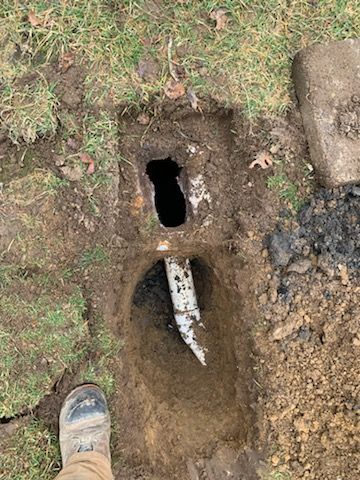 A person is standing in the dirt next to a hole in the ground.