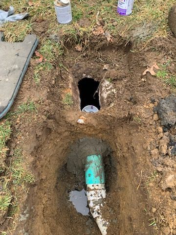 A green pipe is sitting in the dirt next to a hole in the ground.