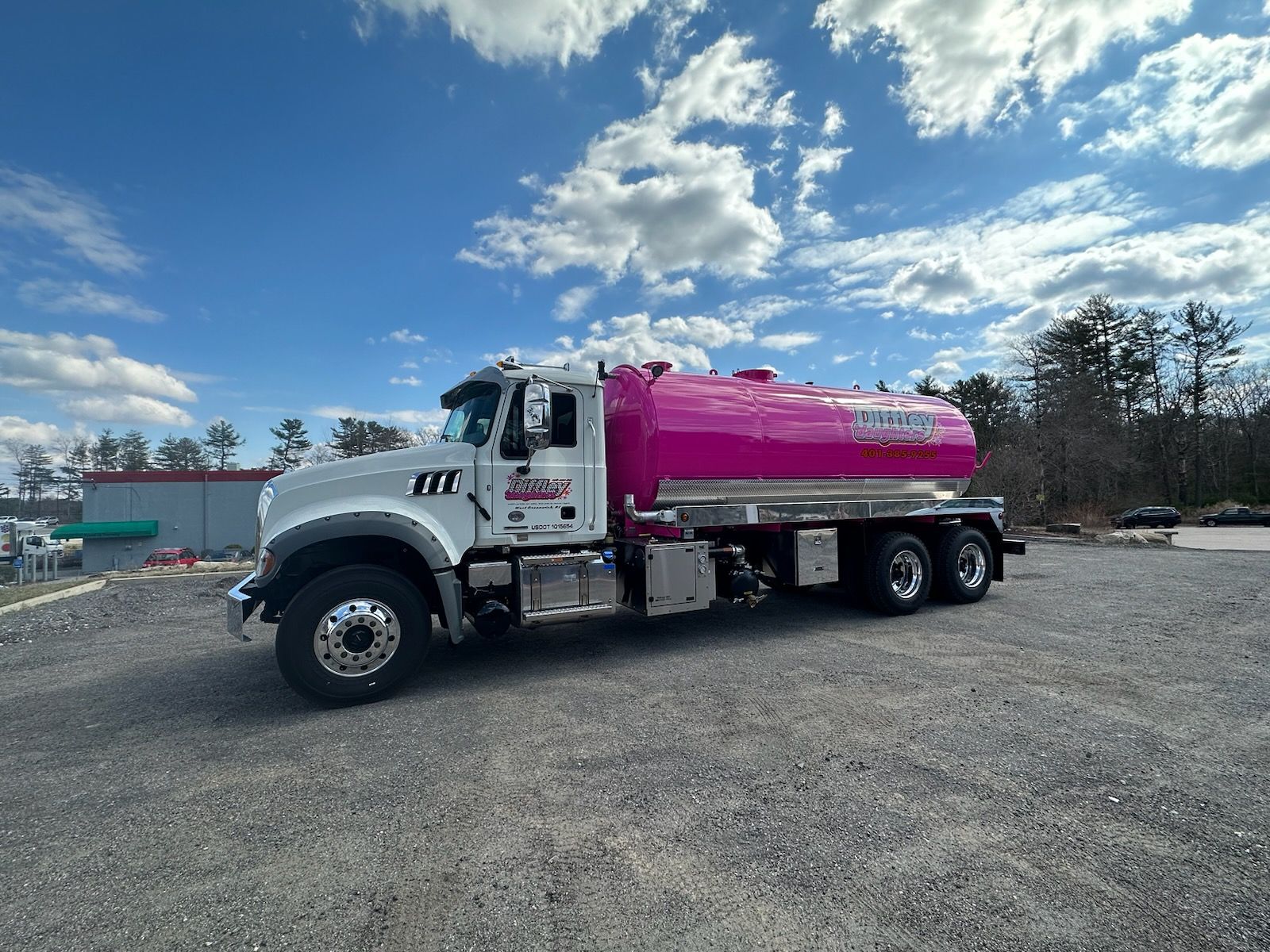 A pink and white tanker truck is parked in a gravel lot.