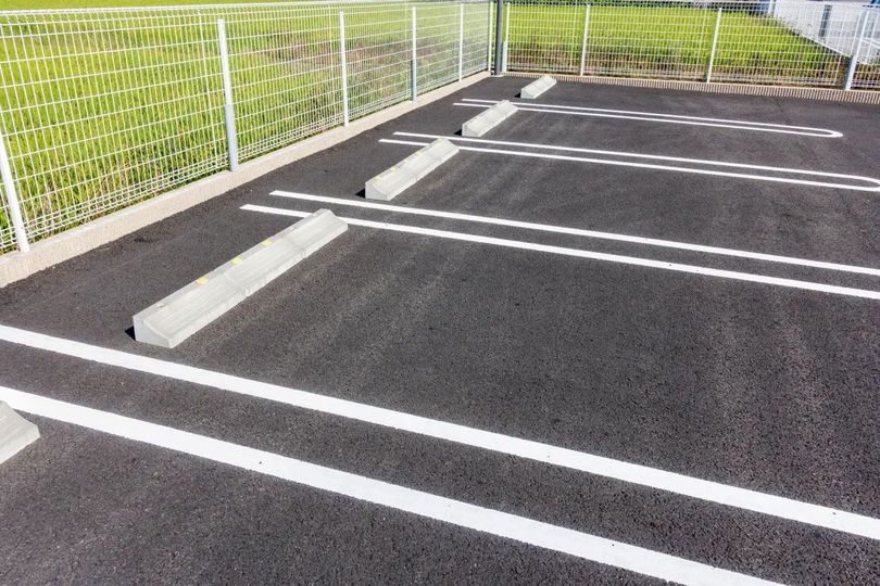Empty parking lot with white lines and concrete wheel stops beside a fence