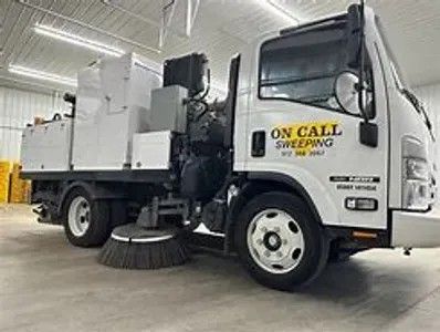 White street sweeper truck in an indoor garage, with “On Call Sweeping” on the door.