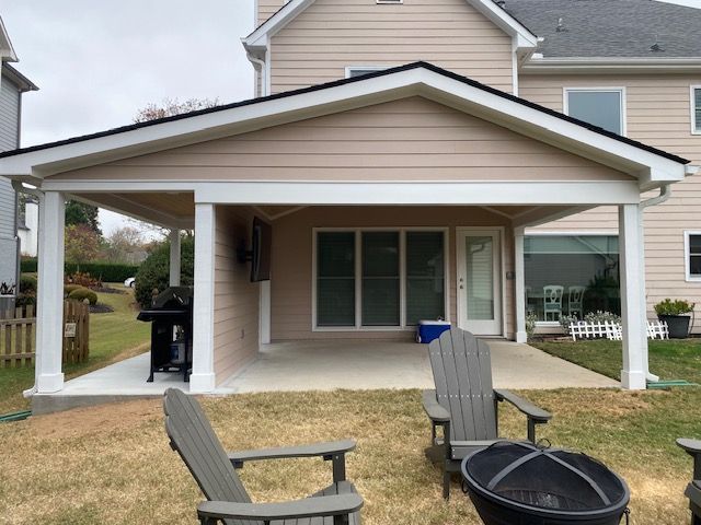 Beige covered patio with chairs, grill, and fire pit in a backyard.