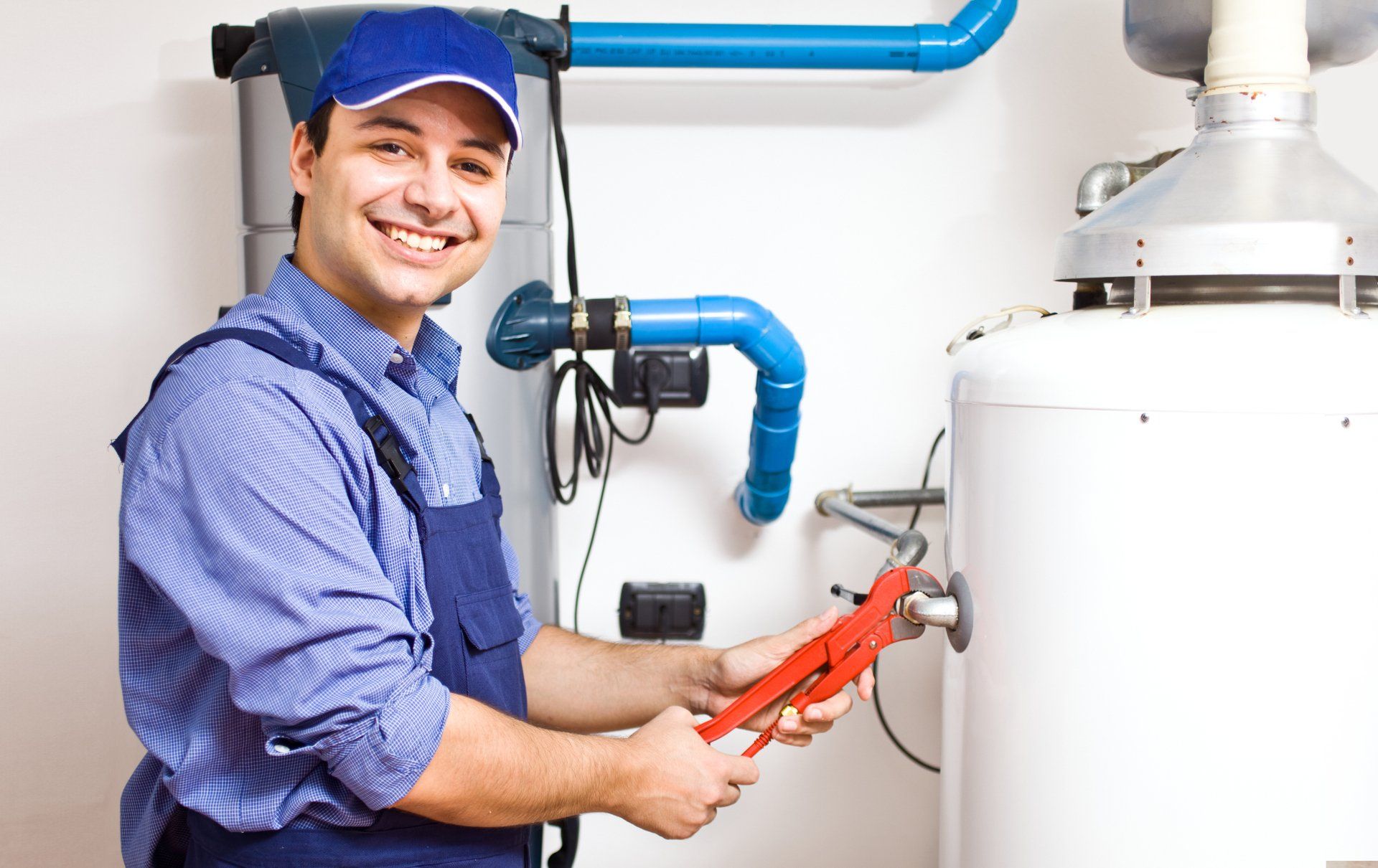 Smiling plumber in blue uniform with wrench fixing water heater.