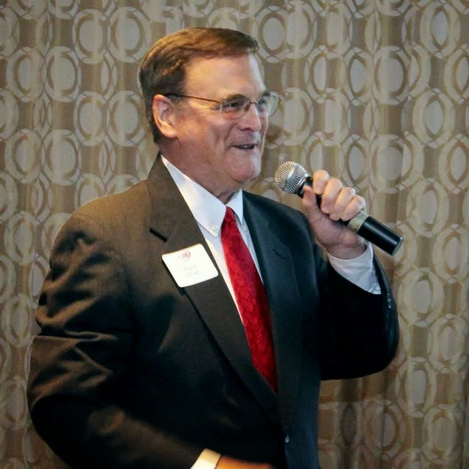 Man in suit, holding microphone, speaking at event.