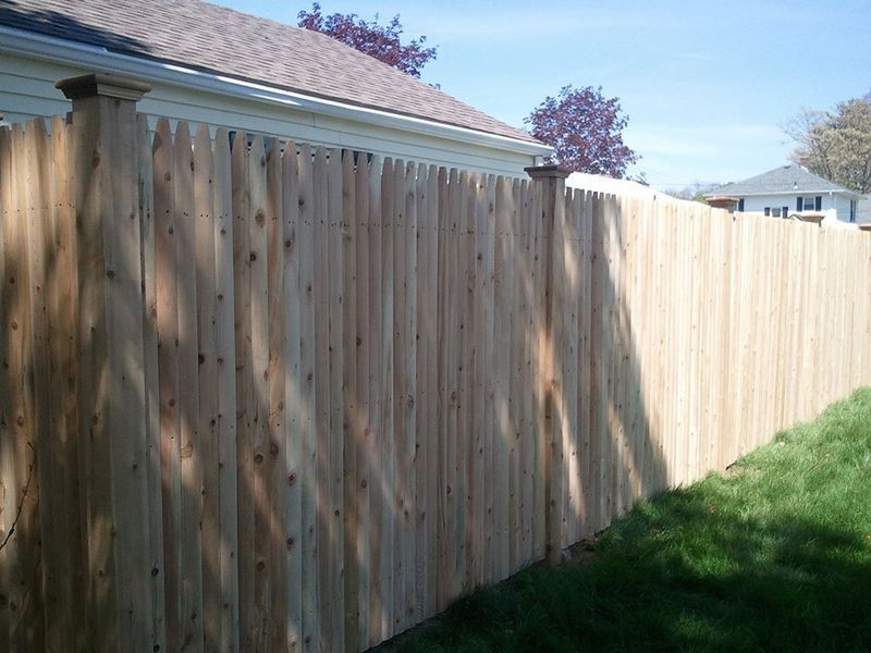 A tall wooden privacy fence with vertical pickets stands in a grassy yard on a sunny day.