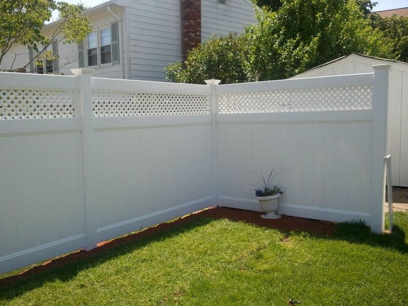 A white vinyl privacy fence with a lattice top forms a corner in a residential backyard with green grass.