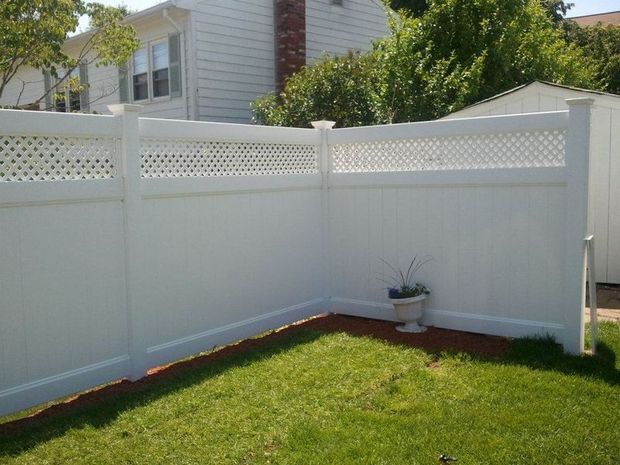 A white vinyl privacy fence with a lattice top section sits in a residential backyard corner next to green grass.