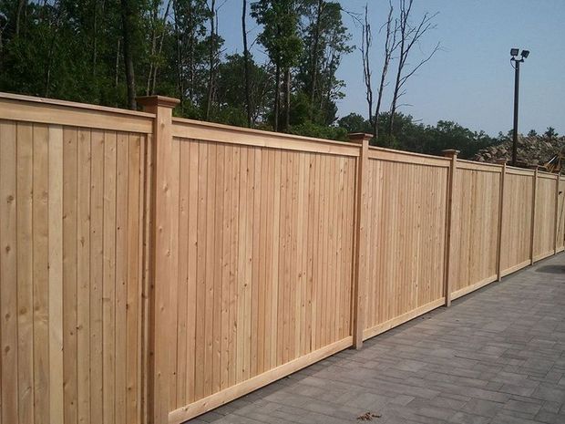A long, sturdy light-brown wooden privacy fence bordering a paved walkway outdoors.